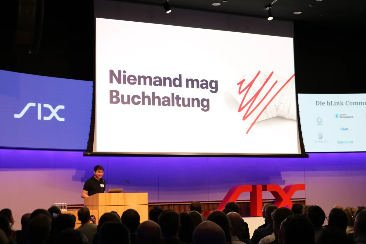 Ein Mann hält eine Präsentation in einem Saal. Im Hintergrund steht auf einer Leinwand: «Niemand mag Buchhaltung».